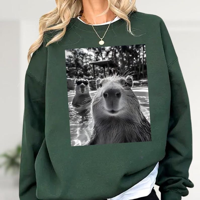 A woman wearing a green sweatshirt with a printed image of two beavers swimming in a pool.