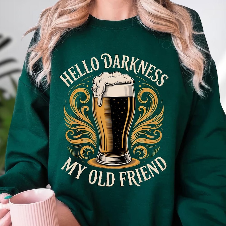 A person wearing a green sweatshirt with a graphic design featuring a beer mug and the text "Hello Darkness, My Old Friend" printed on it.