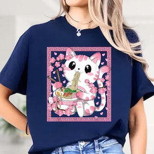 May include: Navy blue t-shirt featuring a cute white cat with pink spots, enjoying ramen. The cat is surrounded by pink cherry blossoms and a pink decorative border. The design is a playful and colorful illustration.