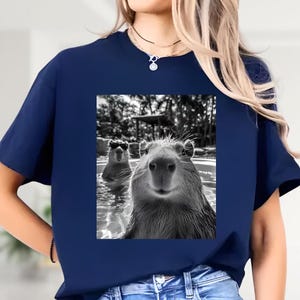 A woman wearing a blue t-shirt with a black and white photograph of two beavers in a pool.