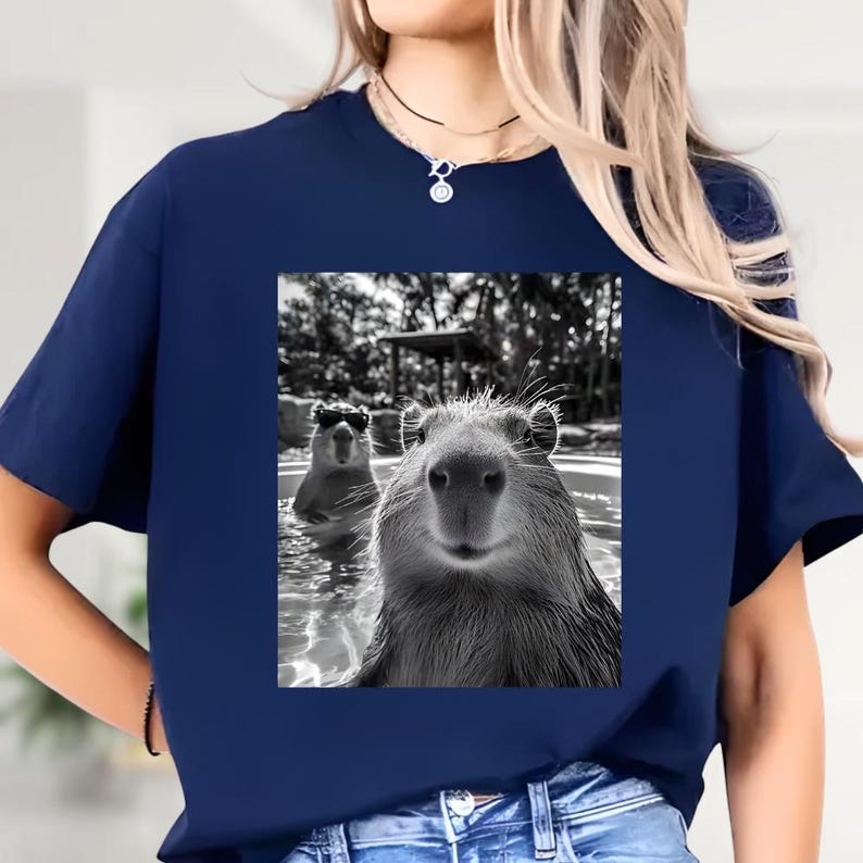 A woman wearing a blue t-shirt with a black and white photograph of two beavers in a pool.