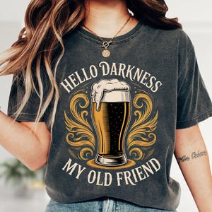 A person wearing a gray t-shirt with a graphic design that says "Hello Darkness, My Old Friend" and features a beer mug with a frothy white head.