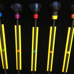 May include: Five black staffs with rounded, textured heads and long, thin yellow foam guards attached to the shafts. Each staff features a distinct coloured band near the head and a secondary coloured accent band further down the black handle.