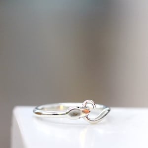 Puede incluir: Un anillo de plata con un dise&ntilde;o de serpiente. La serpiente est&aacute; enroscada con la cola en la boca.