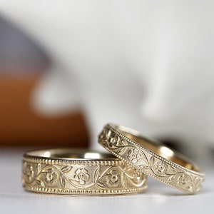 Op de afbeelding: Twee gouden trouwringen met een bloemmotief. De ringen zijn eenvoudig en elegant, met een delicaat bloemmotief.