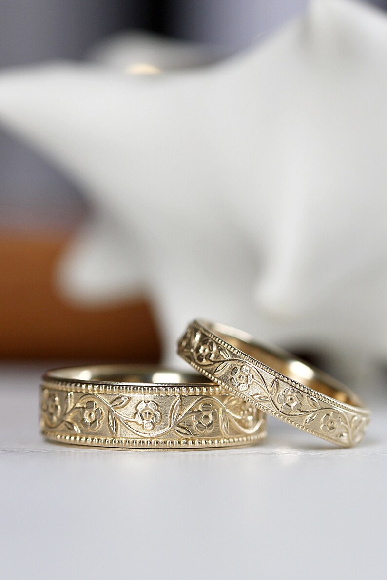 Op de afbeelding: Twee gouden trouwringen met een bloemmotief. De ringen zijn eenvoudig en elegant, met een delicaat bloemmotief.