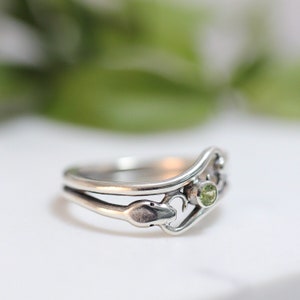 May include: A silver ring with a green gemstone and a snake design.