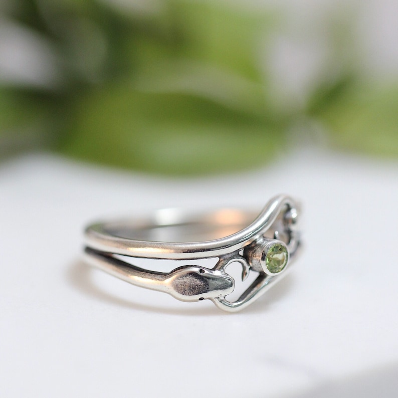 May include: A silver ring with a green gemstone and a snake design.