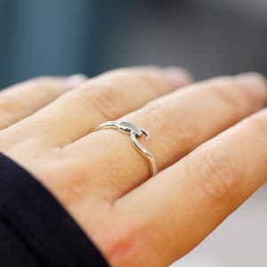 Puede incluir: Un anillo de plata con un dise&ntilde;o de ola. El anillo est&aacute; en el dedo de una persona.