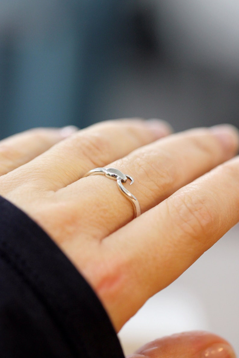 Puede incluir: Un anillo de plata con un dise&ntilde;o de ola. El anillo est&aacute; en el dedo de una persona.