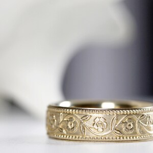 Op de afbeelding: Een gouden trouwring met een bloemmotief. De ring is gegraveerd met een delicaat patroon van bladeren en bloemen.