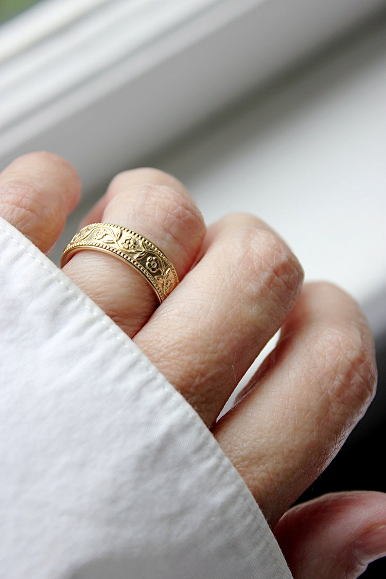 Op de afbeelding: Een gouden ring met een bloemmotief. De ring wordt aan een vinger gedragen.