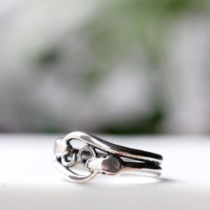 May include: A silver ring with a unique design featuring a snake wrapped around a curved band.
