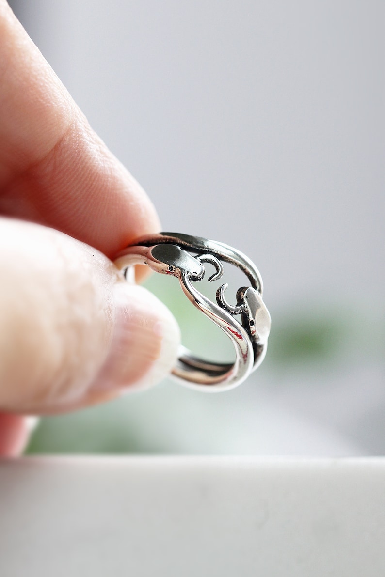 May include: A silver ring with a unique, abstract design. The ring is made of two intertwined bands, creating a delicate and intricate pattern.
