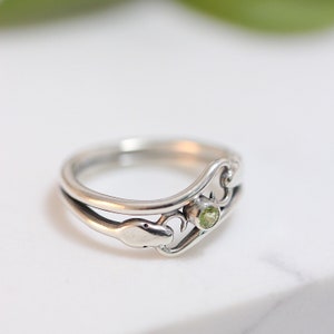 May include: A silver ring with a green gemstone and a snake design.