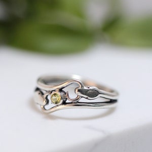 May include: A silver ring with a delicate design featuring a small green gemstone and a snake-like detail.