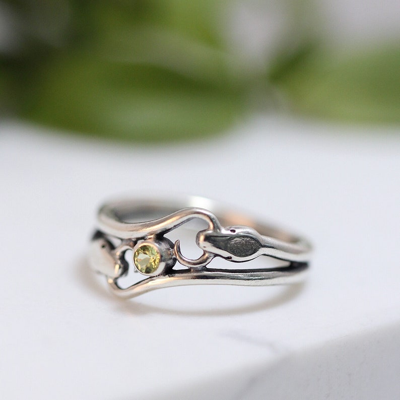 May include: A silver ring with a delicate design featuring a small green gemstone and a snake-like detail.