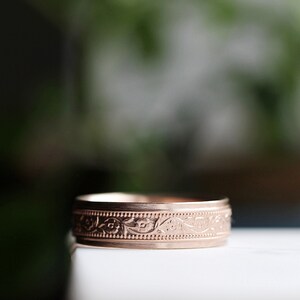 May include: A rose gold band ring with a floral design engraved around the band.