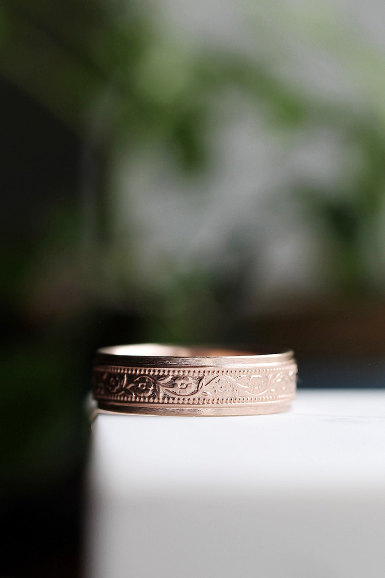 May include: A rose gold band ring with a floral design engraved around the band.