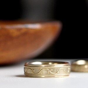 May include: A gold wedding band with a delicate vine design.
