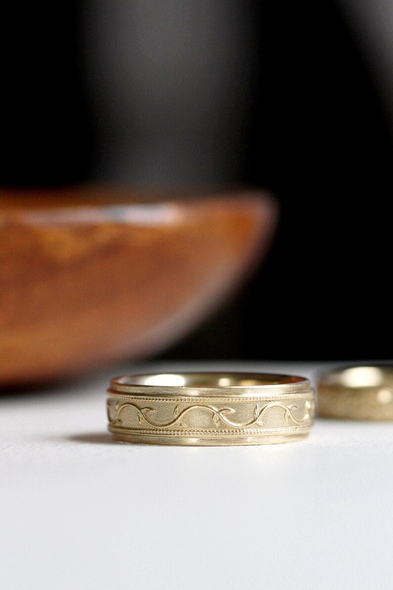 May include: A gold wedding band with a delicate vine design.