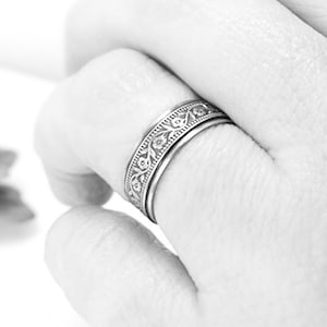 May include: A silver ring with a floral design. The ring is worn on a finger.