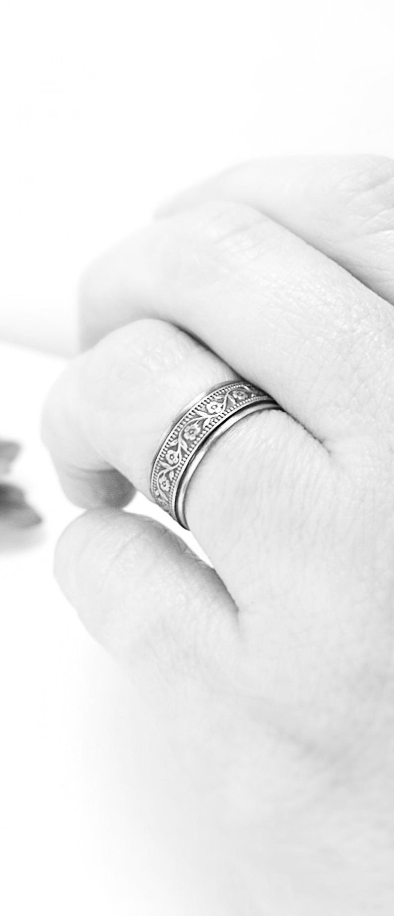 May include: A silver ring with a floral design. The ring is worn on a finger.