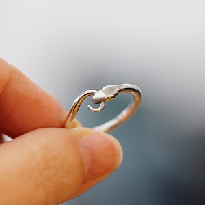 Puede incluir: Un anillo de plata con un dise&ntilde;o de serpiente. La cabeza de la serpiente est&aacute; enroscada y el anillo est&aacute; abierto en la parte posterior.