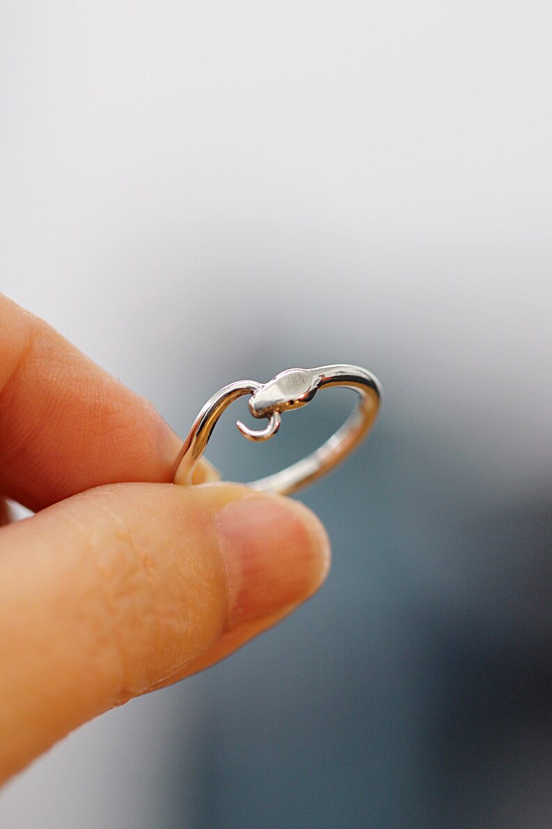 Puede incluir: Un anillo de plata con un dise&ntilde;o de serpiente. La cabeza de la serpiente est&aacute; enroscada y el anillo est&aacute; abierto en la parte posterior.