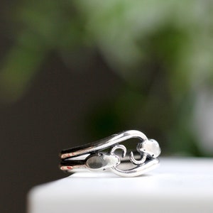 May include: A silver ring with a delicate, openwork design featuring two stylized leaves. The ring is made of polished silver and has a smooth, rounded band.