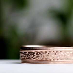 May include: A close-up of a rose gold wedding band with a floral design.