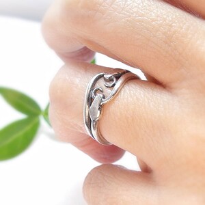 May include: A silver ring with a unique, intricate design featuring a swirling pattern. The ring is worn on a finger.