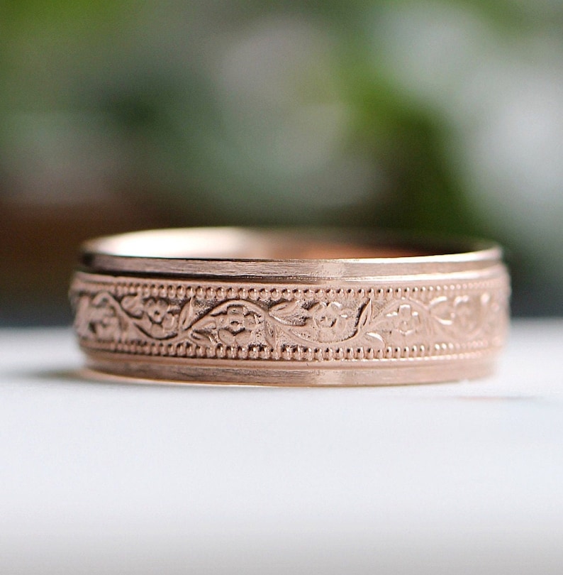 May include: A rose gold wedding band with a floral engraved design.