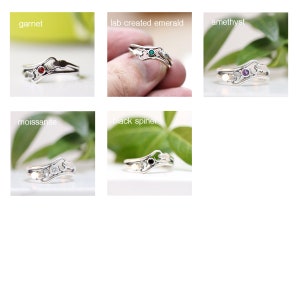 May include: Six silver rings with different gemstones. The rings feature a delicate, swirling design with a small gemstone set in the center. The gemstones are garnet, lab created emerald, amethyst, moissanite, black spinel.