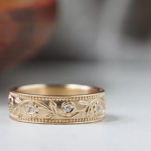 Op de afbeelding: Een gouden band met een bloemmotief en kleine diamanten. De band is gegraveerd met een wijnstok en bloemen.