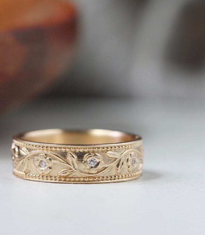 Op de afbeelding: Een gouden band met een bloemmotief en kleine diamanten. De band is gegraveerd met een wijnstok en bloemen.