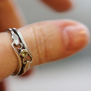 May include: A silver ring with a green gemstone set in a delicate design. The ring is worn on a finger.
