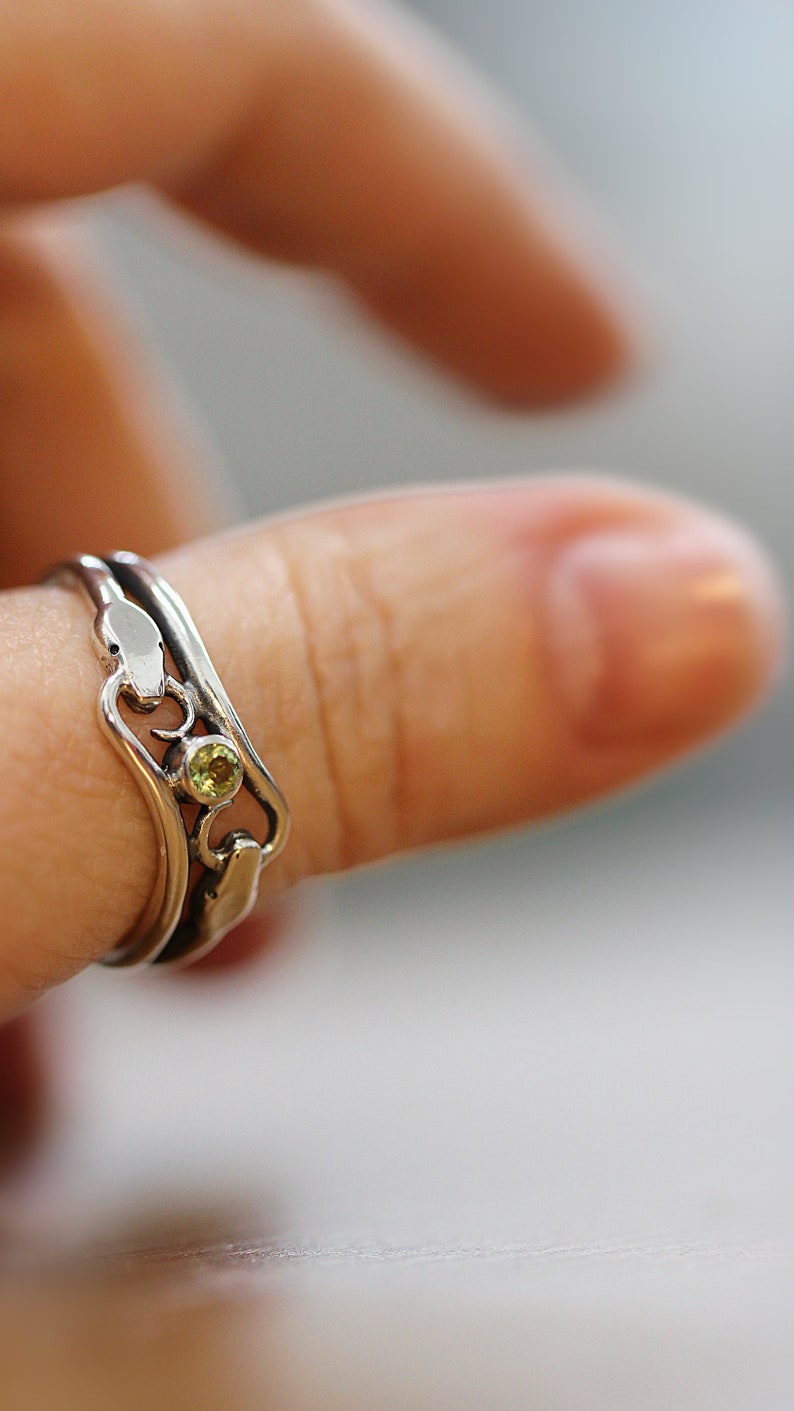 May include: A silver ring with a green gemstone set in a delicate design. The ring is worn on a finger.