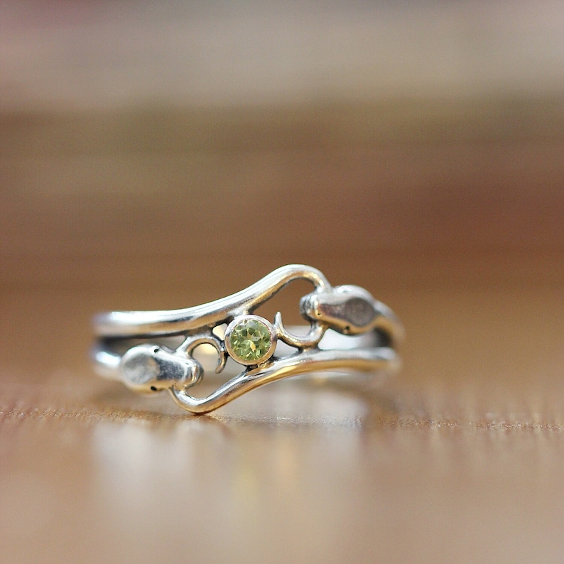 May include: A silver ring with a delicate design featuring a green gemstone. The ring has a curved shape and a floral motif.