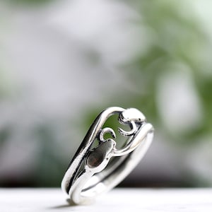 May include: A silver ring with a delicate, intricate design. The ring features a wave-like band with a stylized floral motif.