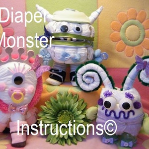 May include: Three diaper monster toys, each with a different design. The first is a white monster with green and blue accents, the second is a pink and white monster with a crown, and the third is a purple and white monster with green and purple accents. The toys are all made from diapers and other baby supplies.