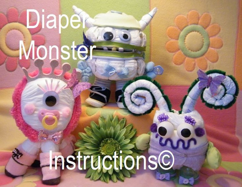 May include: Three diaper monster toys, each with a different design. The first is a white monster with green and blue accents, the second is a pink and white monster with a crown, and the third is a purple and white monster with green and purple accents. The toys are all made from diapers and other baby supplies.