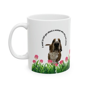 May include: White ceramic mug with a brown and white basset hound dog in a field of green grass and pink tulips. The text on the mug reads "I want to tell you about a woman who only eats plants."