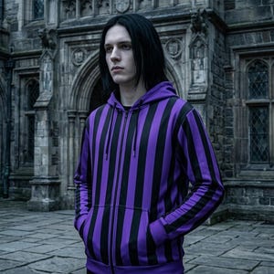 May include: A person wearing a purple and black striped zip-up hoodie. The hoodie has a hood and pockets. The person is standing in front of a stone building with arched windows and doors.