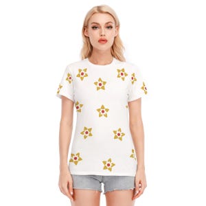 Könnte beinhalten: Weißes T-Shirt mit einem sich wiederholenden Muster aus goldenen Sternen mit roten Zentren. Das kurzärmelige Shirt ist aus einem weichen Material gefertigt und eignet sich für Freizeitkleidung. Das Shirt wird mit Jeansshorts kombiniert.