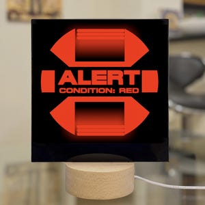 May include: A black and red light-up sign with the text "ALERT CONDITION: RED" in a white font. The sign is shaped like a cross with a red light in the center.