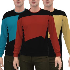 May include: Three long-sleeved shirts with a black background and a coloured geometric shape on the front. The shirts are teal, red, and gold.