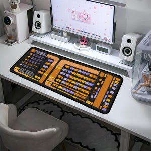 Può includere: Un tappetino da scrivania nero e arancione con un design ispirato a Star Trek. Il tappetino presenta un pannello di controllo con pulsanti ed etichette, tra cui "Food Service".