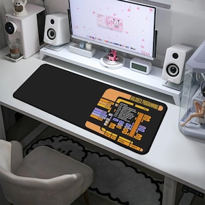 May include: A black desk mat with a Star Trek themed design. The design features a yellow and orange control panel with the text "HOLODECK PROGRAMMING".