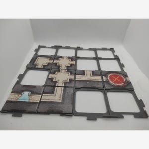 Puede incluir: Baldosas de juego modulares en gris y beige. Las baldosas presentan varios diseños, incluyendo un emblema circular con borde rojo y un elemento arquitectónico azul y blanco. Las baldosas están diseñadas para entrelazarse.